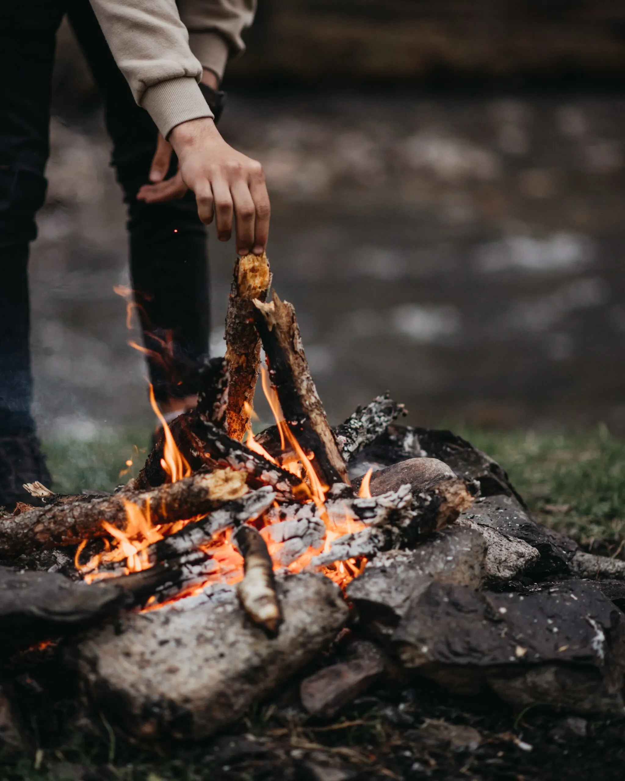 Unrecognizable man burning firewood near lake